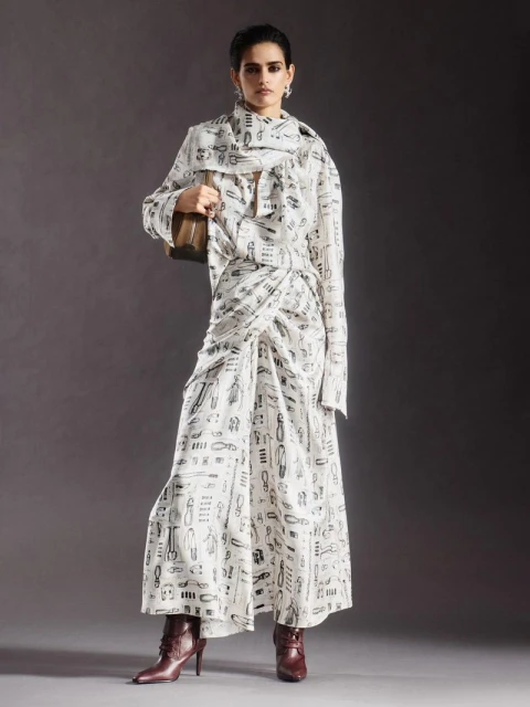 Full-length shot of an adult female wearing a printed white two-piece outfit and burgundy ankle boots against a grey backdrop.