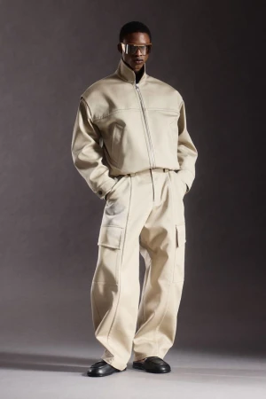 Model Nonso Ojukwu wearing a beige structured zip-up jacket, wide cargo pants, and visor sunglasses for Ferrari.