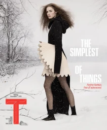 Model Sarah Isaksen posing in a snowy landscape wearing a black knit hooded dress with a sculptural pleated cream skirt.