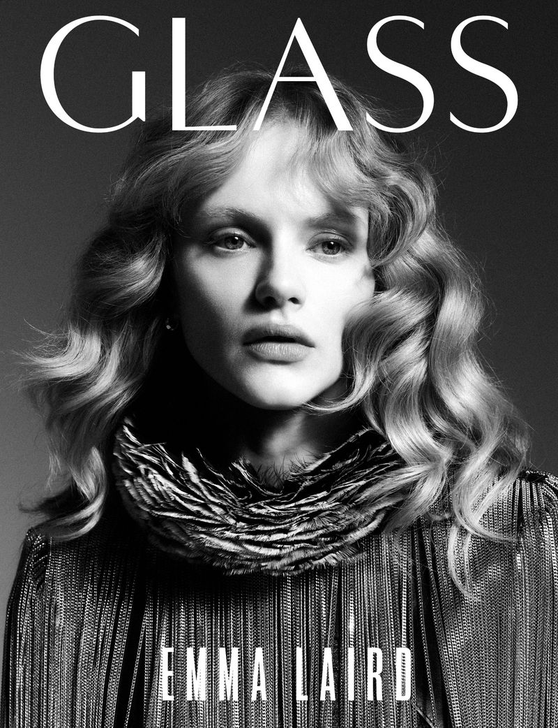 Black and white portrait of a woman with wavy blonde hair, wearing a fringe dress and feathered neckpiece, featured on the cover of GLASS.