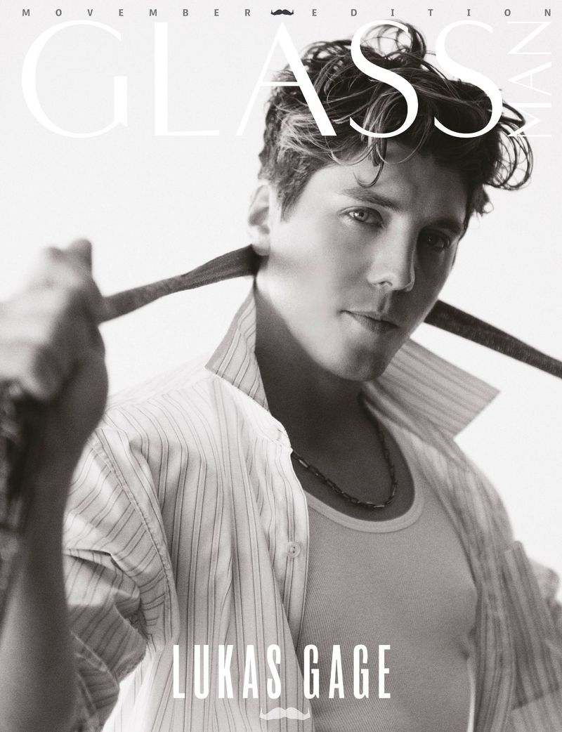 Black and white magazine cover of Lukas Gage in an unbuttoned shirt and tie around his neck, shot with soft light.