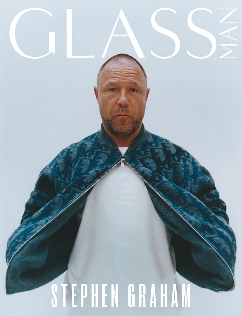 Stephen Graham on a Glass Man magazine cover, wearing a blue patterned bomber jacket, standing against a pale grey backdrop.