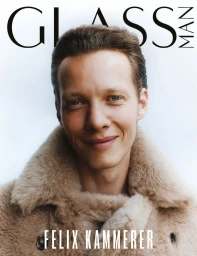 Actor Felix Kammerer smiling in a plush beige shearling coat on the cover of Glass Man Magazine against a white backdrop.