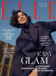 Model with dark short hair wearing a navy coat and turtleneck against a blue sky and building exterior
