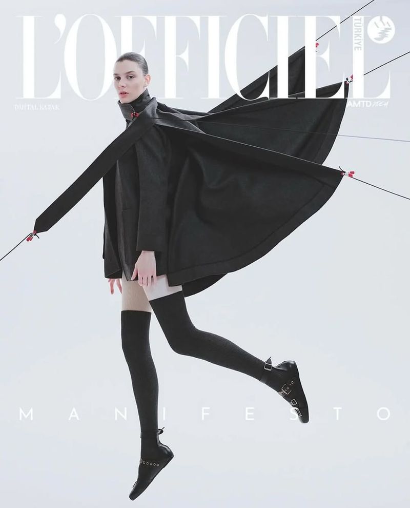 Fashion editorial cover featuring a woman in black coat and stockings, posed dynamically against a light background with minimalist design.