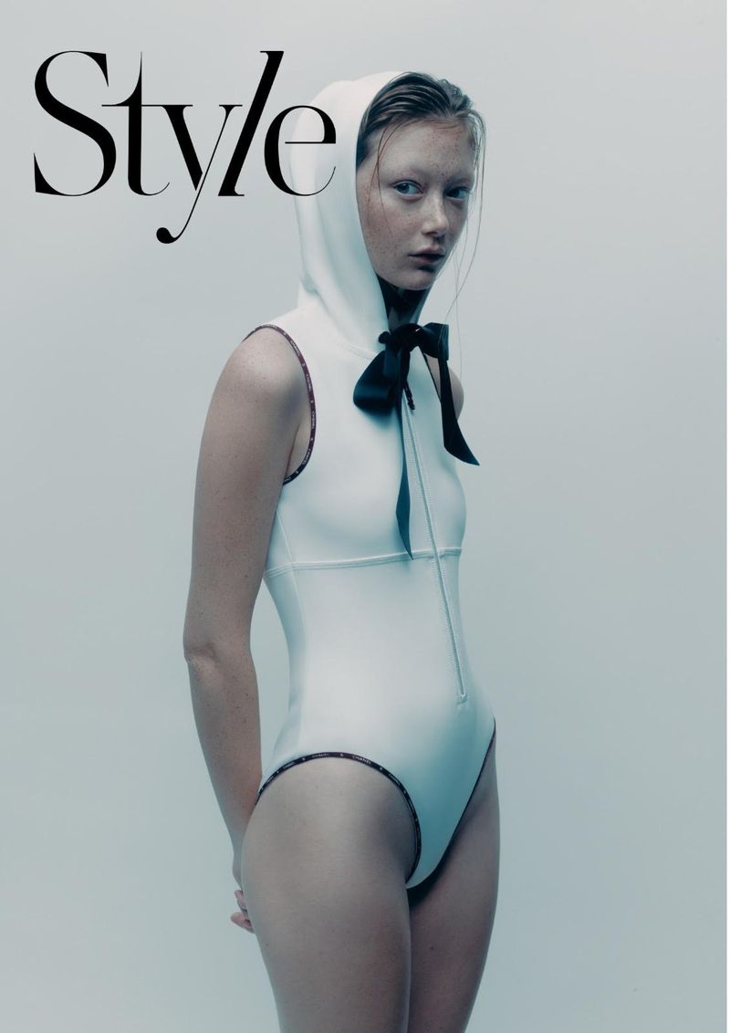 Fashion magazine cover featuring a slender adult female model in a white hooded bodysuit with a large black bow, against a pale background.