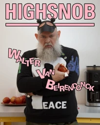 Man with long grey beard wearing a black graphic sweatshirt and horned headwear holding an apple in a kitchen