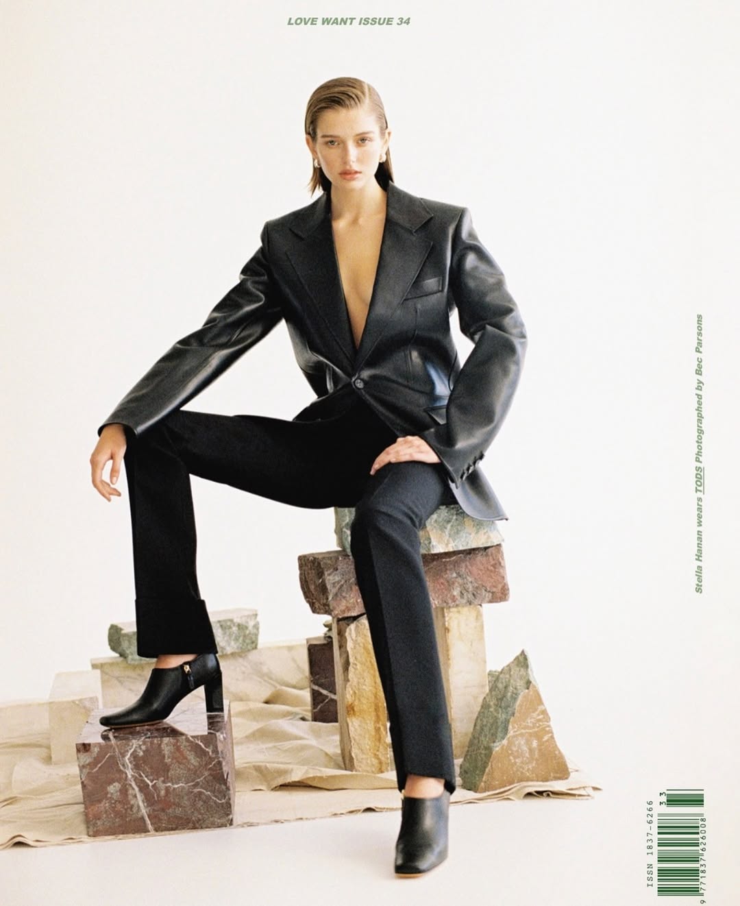 A fashion magazine cover features a model in a black blazer and pants sitting on stone blocks in front of a white backdrop.