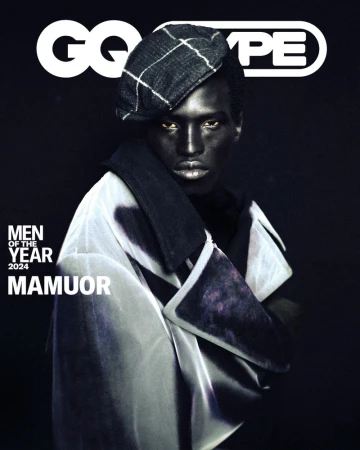 Portrait of Black man, Mamour, wearing a beret and draped coat, GQ cover with black backdrop. Fashion editorial portrait.