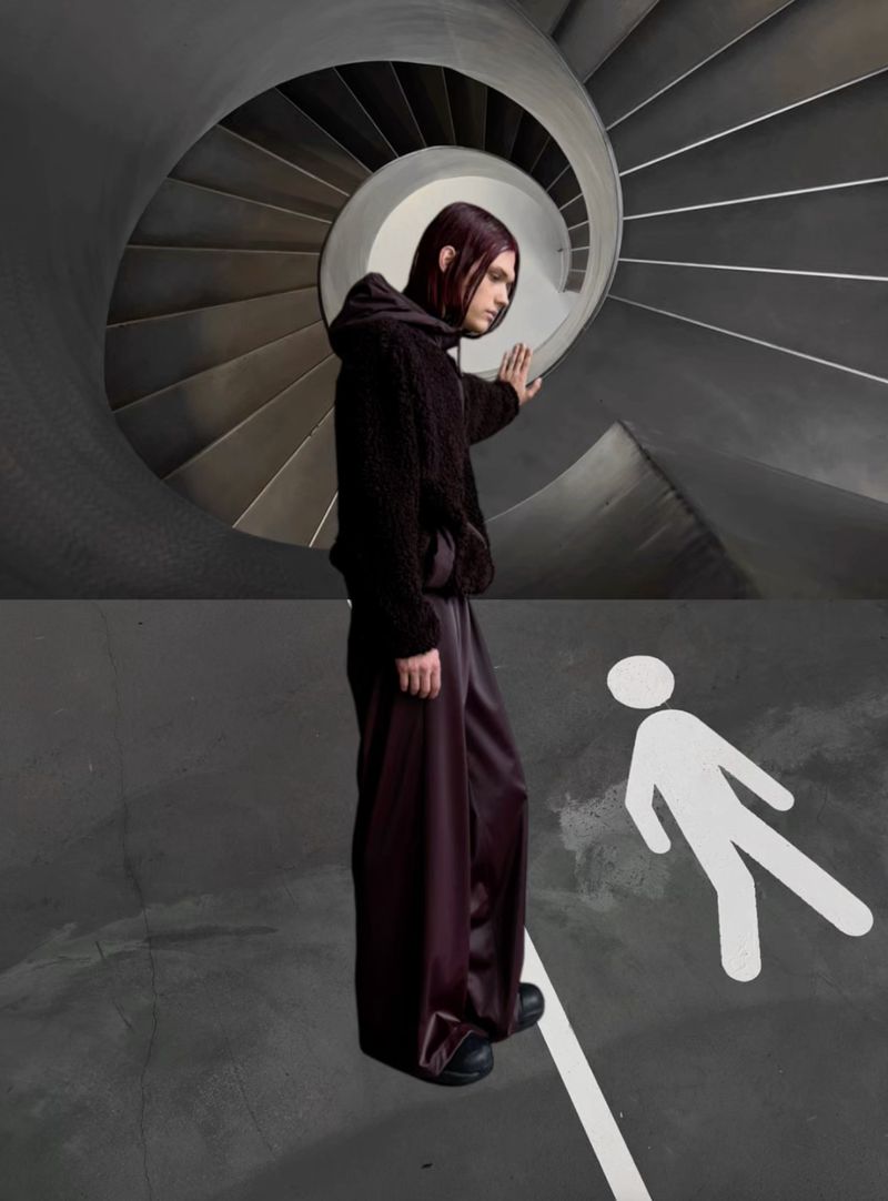 A person stands in front of a pedestrian crossing symbol and a spiraling staircase in an abstract studio-lit fashion shot.