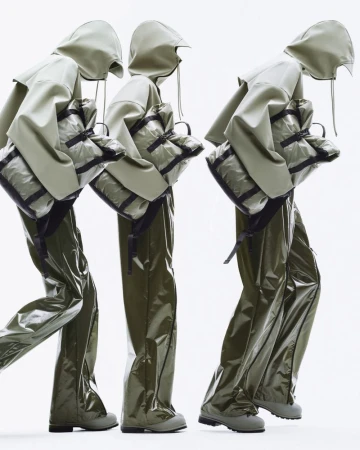 Three figures in olive green hooded raincoats and trousers, each carrying a matching bag, against a bright white backdrop.