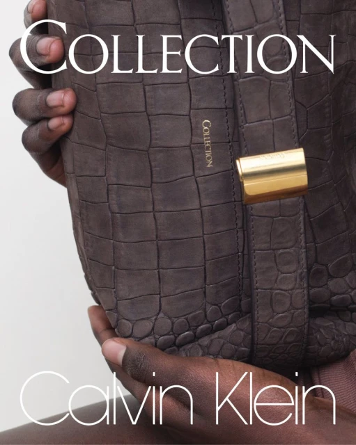 Close up of a brown leather Calvin Klein purse with gold hardware held by a person in front of a light gray background.