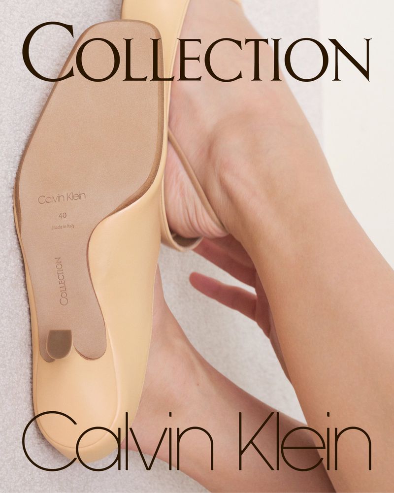 Elevated view of a beige Calvin Klein mule with a slender heel, paired with a foot, against a soft, neutral backdrop.