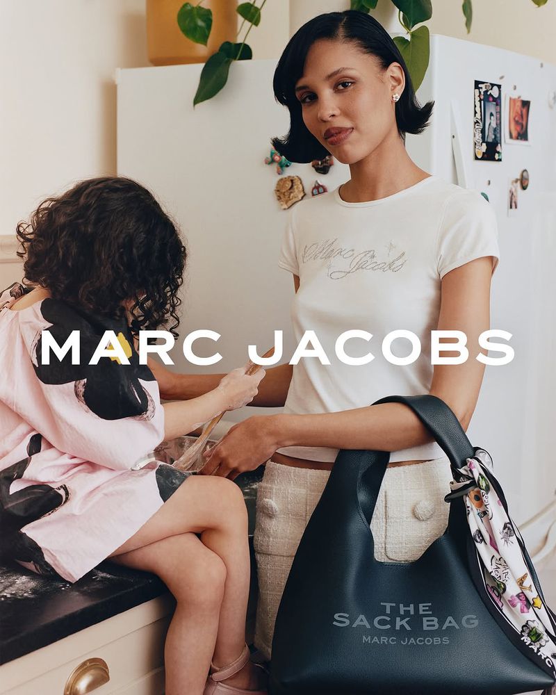 A woman and a child in a kitchen setting, next to a black Marc Jacobs Sack Bag; interior kitchen setting, natural light.