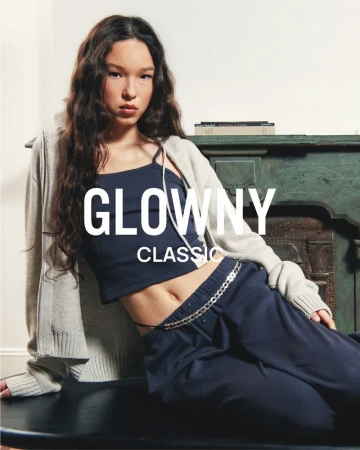 Model wearing dark blue tank top and pants with cream cardigan posing against a green mantelpiece
