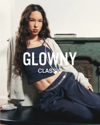 Model wearing dark blue tank top and pants with cream cardigan posing against a green mantelpiece