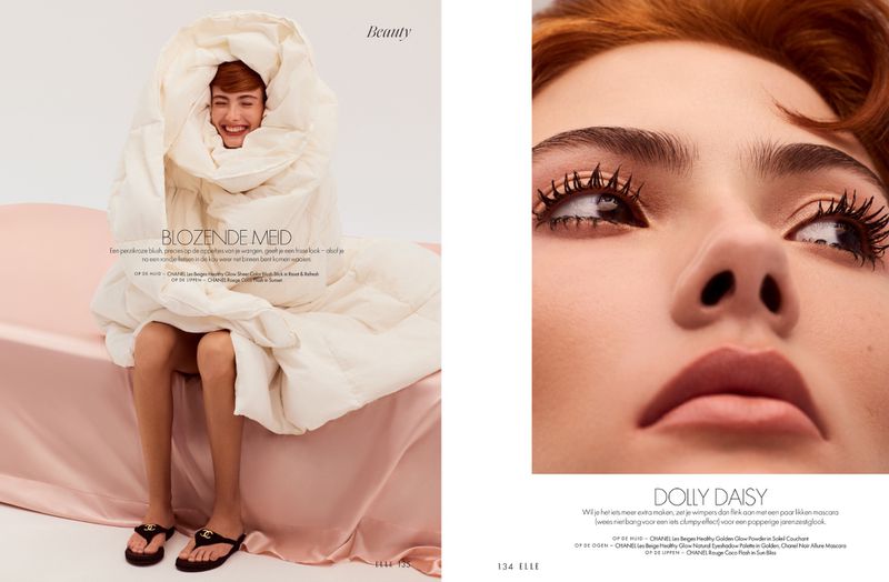 Model wrapped in duvet, reclined on bed, smiles for beauty ad. Close-up of model with striking mascara enhances eye makeup look.