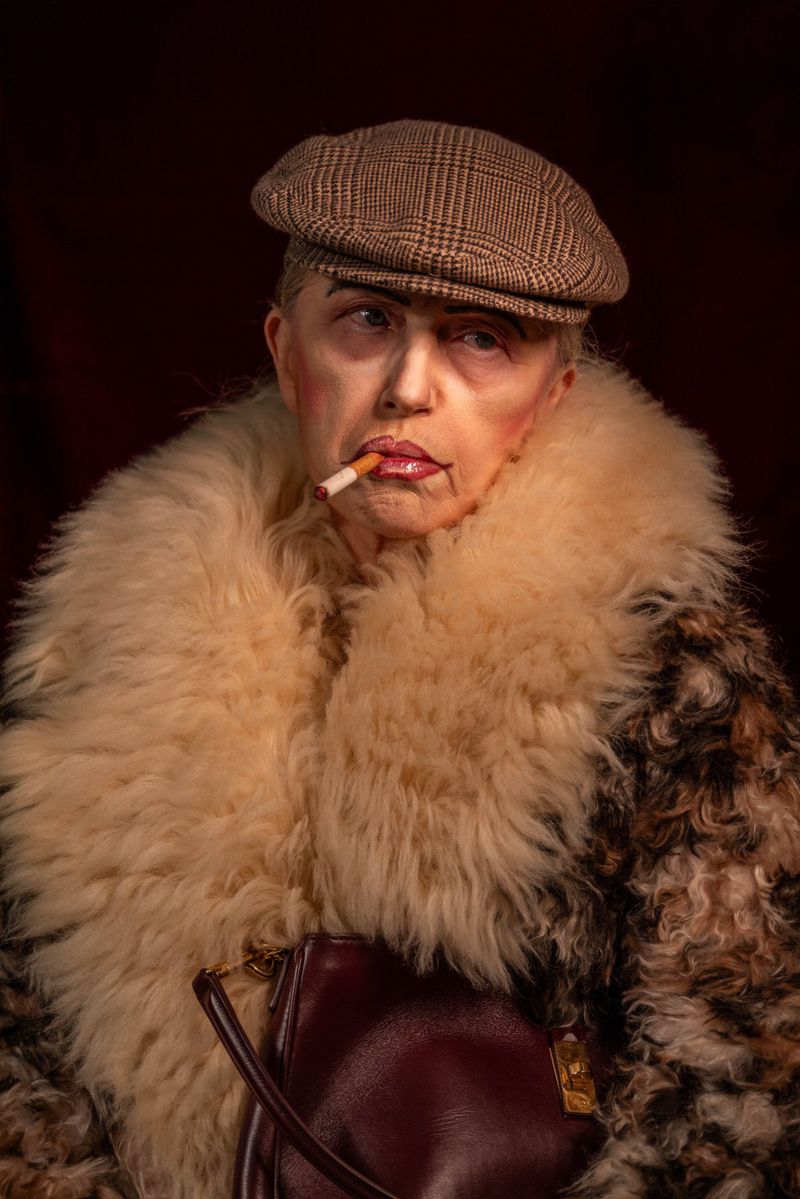 Elegant woman in a fur coat and cap poses indoors with a cigarette, creating a vintage and stylish visual narrative.