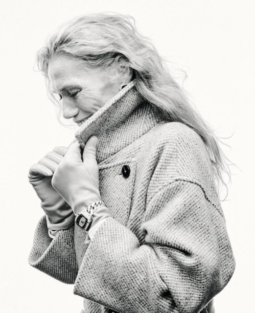 Elegant elderly woman in tweed coat and gloves looking down in black and white studio shot. Classic watch on wrist. Clean, bright background.