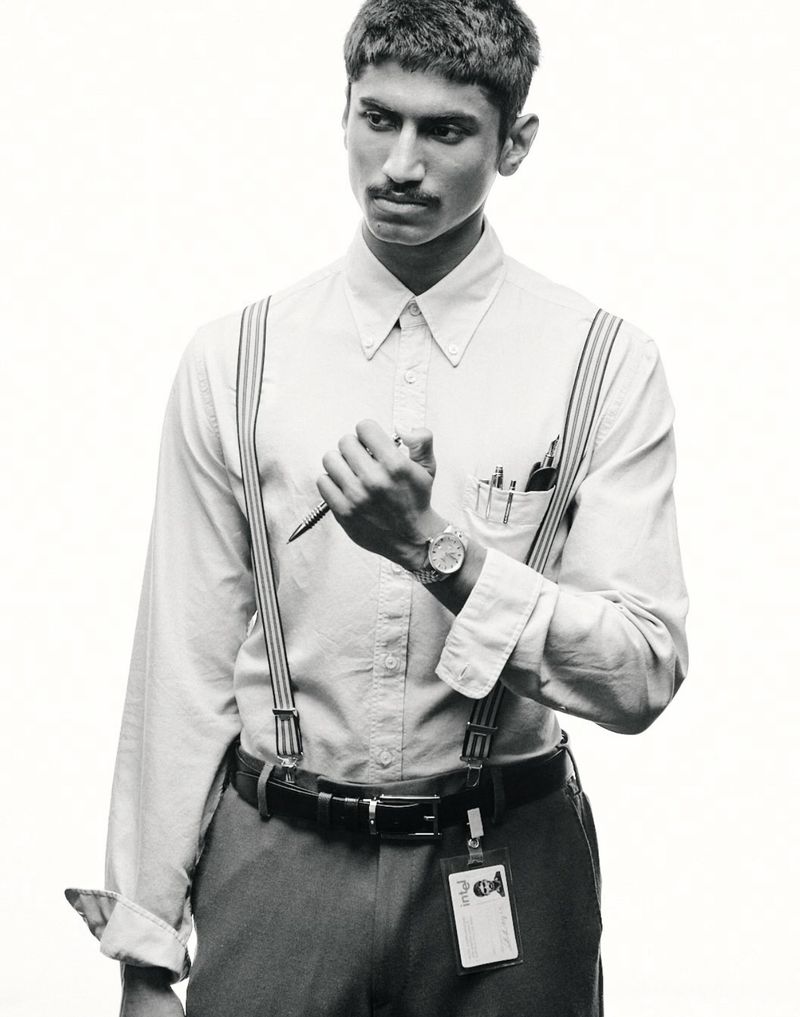 Black and white portrait of a young adult man in a button-down shirt and suspenders, holding a pen and looking off to the side.