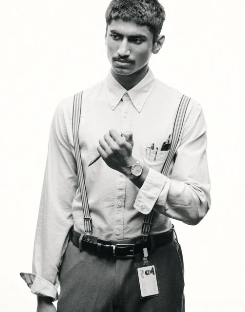 Black and white portrait of a young adult man in a button-down shirt and suspenders, holding a pen and looking off to the side.