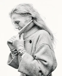 Elderly woman in tweed coat and leather gloves smiling against a white background