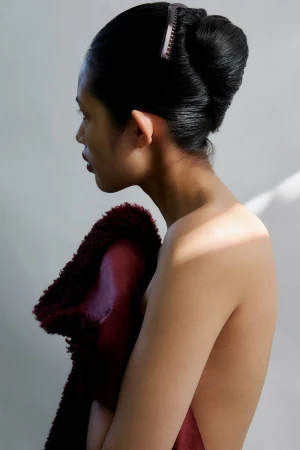Profile view of an Asian adult woman with dark hair in an updo and hair comb, partially draped with a burgundy furry textile.