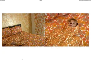Model Anthony Foster lies on floral bedding wearing a matching orange and yellow floral hooded parka in a bedroom editorial.