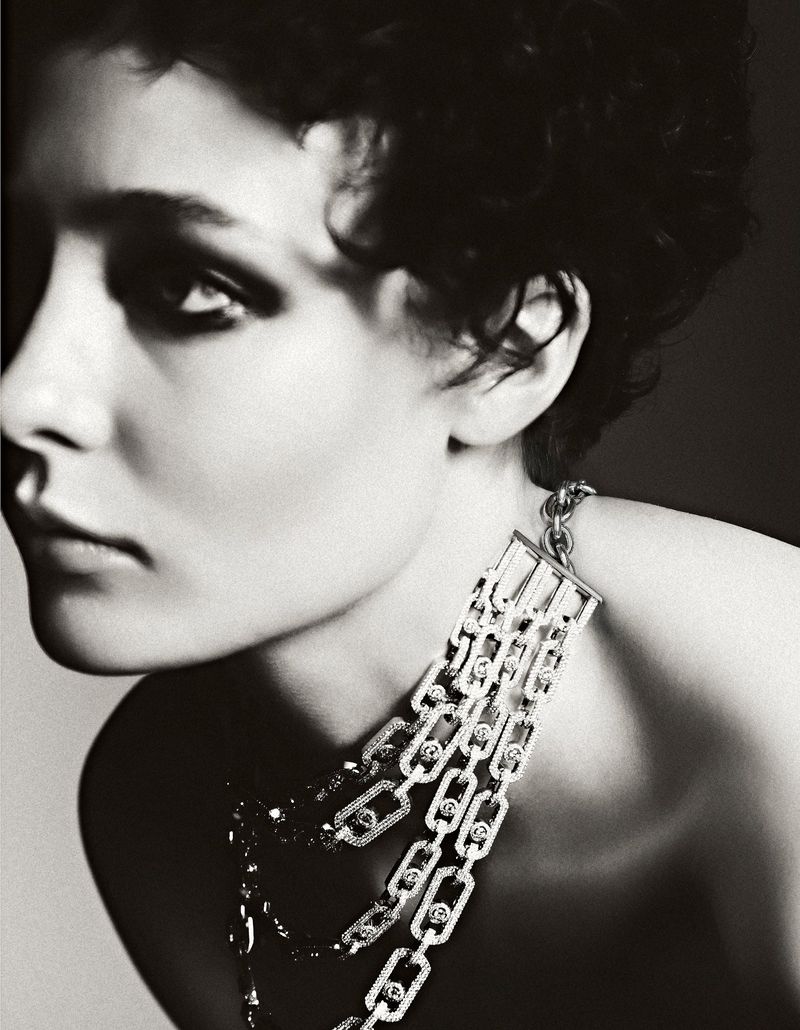 Monochrome portrait of a woman with short dark hair wearing a silver and diamond necklace against a light grey background.