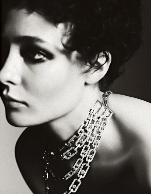 Monochrome portrait of a woman with short dark hair wearing a silver and diamond necklace against a light grey background.
