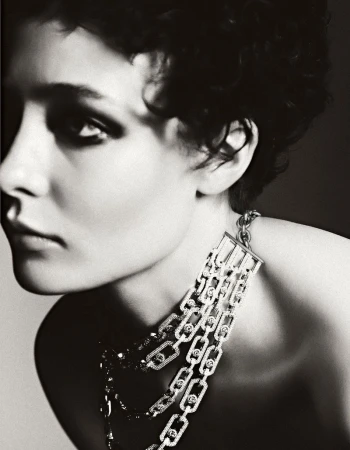 Monochrome portrait of a woman with short dark hair wearing a silver and diamond necklace against a light grey background.