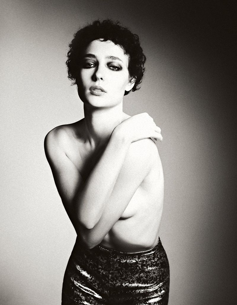 Monochrome portrait of a woman with dark curly hair in metallic pants. Woman poses against a diffused studio background in soft light.
