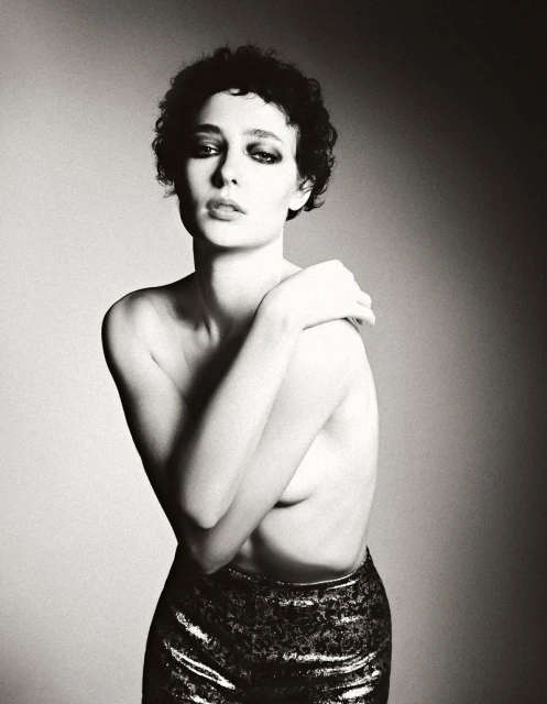 Monochrome portrait of a woman with dark curly hair in metallic pants. Woman poses against a diffused studio background in soft light.