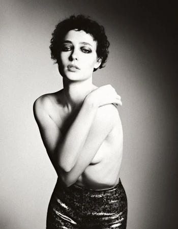 Monochrome portrait of a woman with dark curly hair in metallic pants. Woman poses against a diffused studio background in soft light.