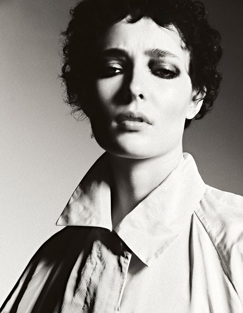 Monochrome portrait of a person with dark curly hair wearing a collared shirt, featuring a soft light and neutral background.