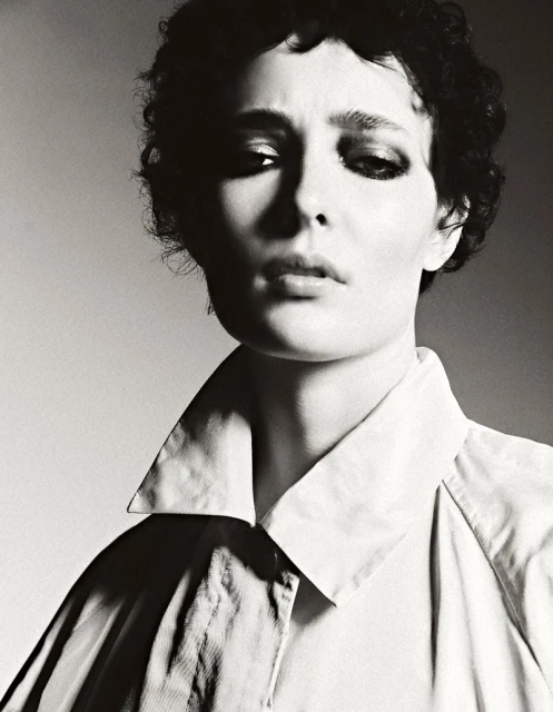 Monochrome portrait of a person with dark curly hair wearing a collared shirt, featuring a soft light and neutral background.