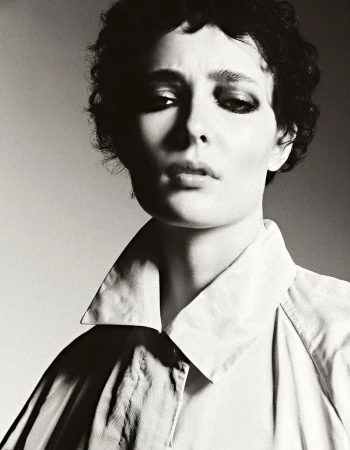 Monochrome portrait of a person with dark curly hair wearing a collared shirt, featuring a soft light and neutral background.