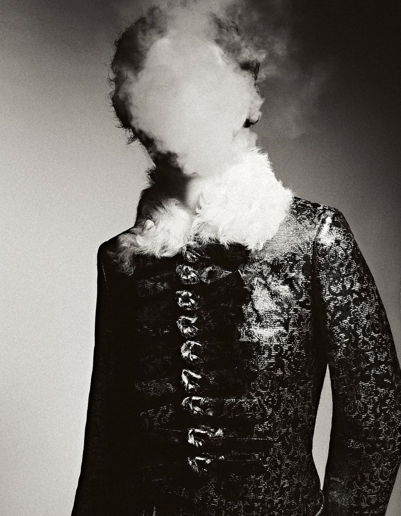 Monochrome portrait of a person in an ornate jacket with a fur collar, face obscured by a cloud of smoke, creating a mysterious aesthetic.