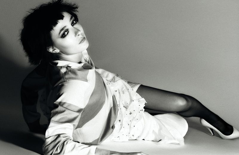 Elegant woman with dark hair and dress posing in a studio, black and white portrait with white high heels and sheer stockings.