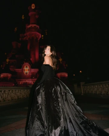 Model in a voluminous black ballgown with matching gloves posing outdoors at night against a castle backdrop