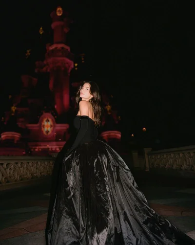 Model in a voluminous black ballgown with matching gloves posing outdoors at night against a castle backdrop
