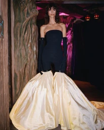 Model wearing a strapless black jumpsuit with matching gloves and voluminous yellow skirt panels