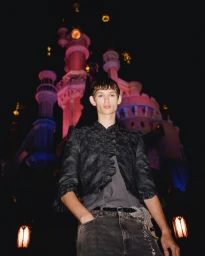 Model standing outdoors at night in front of an illuminated castle under Coperni S/S 25 Disneyland project