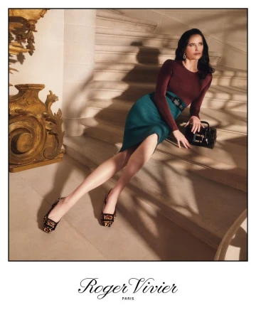 Elegant woman in long-sleeved maroon top and teal pencil skirt poses on stairs with a black purse and decorative shoes.