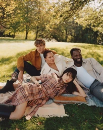 Group of four people relaxing on a plaid blanket in a grassy park setting under trees for Burberry.