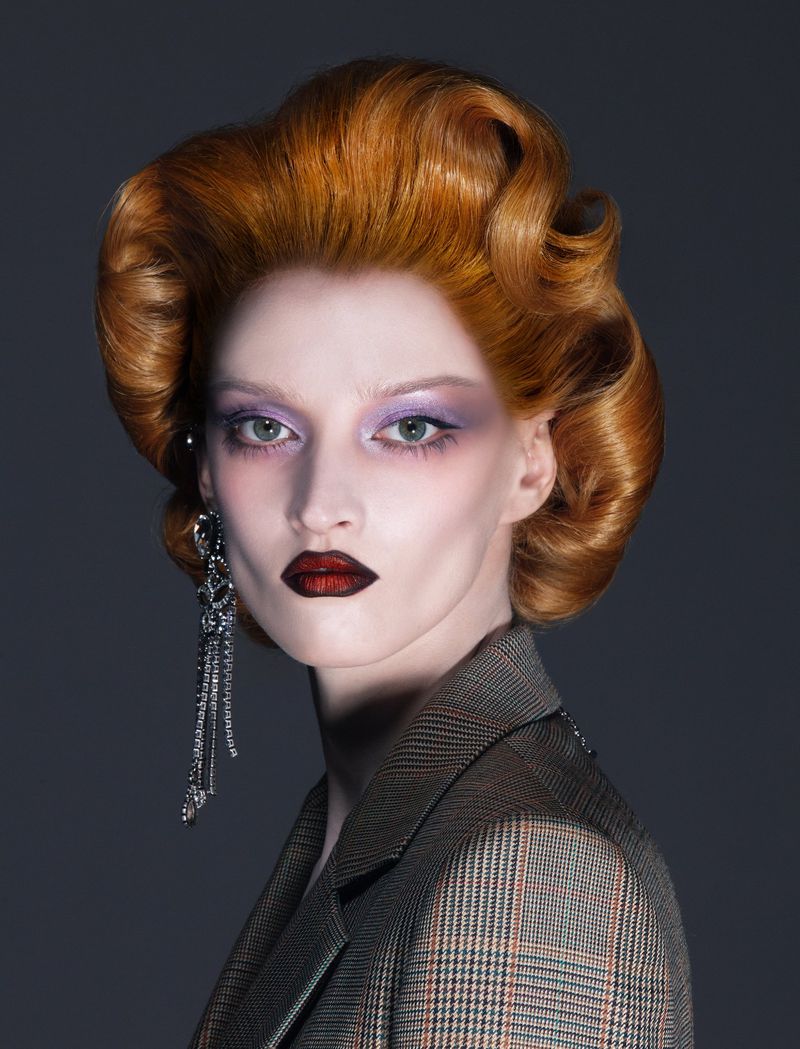 Elegant woman with vintage hair and statement earrings poses in a professional studio wearing a stylish plaid blazer. Beauty shot.