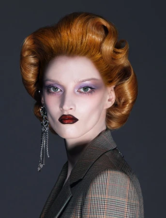 Elegant woman with vintage hair and statement earrings poses in a professional studio wearing a stylish plaid blazer. Beauty shot.