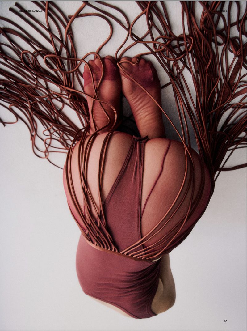 Back and feet of a person in a maroon swimsuit and matching hosiery. Many strands of maroon fabric cover the body in a studio shot.
