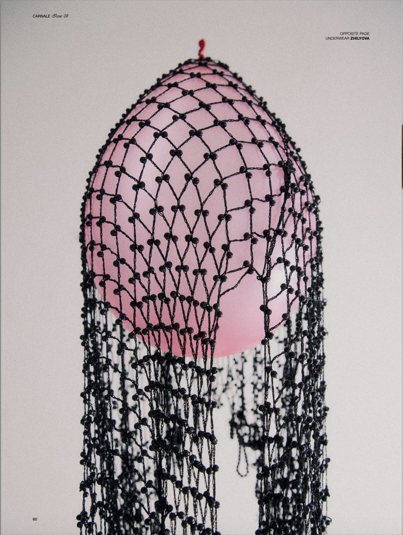 Stylized close-up of a pink balloon covered in black beaded netting and photographed against a light grey seamless backdrop.