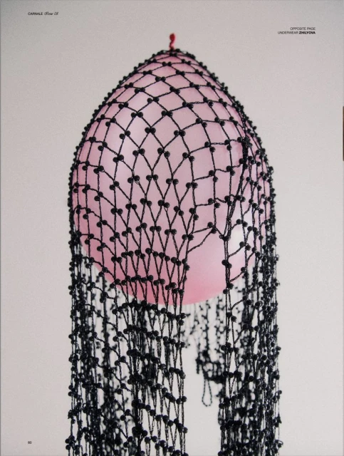 Stylized close-up of a pink balloon covered in black beaded netting and photographed against a light grey seamless backdrop.